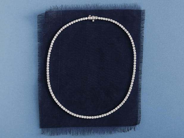 Diamond necklace on navy blue fabric with light blue background.