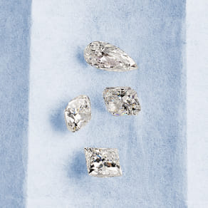 Four sparkling diamonds with different cuts displayed on a blue surface.