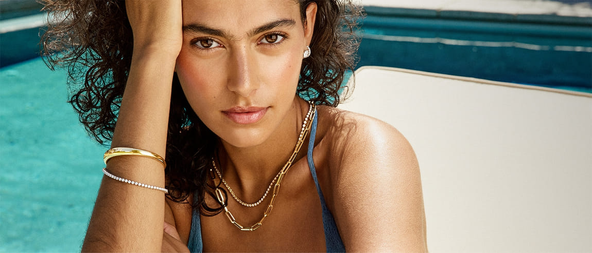 Woman by a pool wearing gold jewelry and a blue swimsuit.