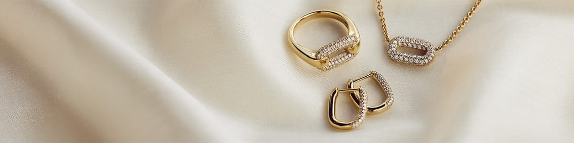 Gold ring, earrings, and necklace with diamond accents on a soft fabric background.