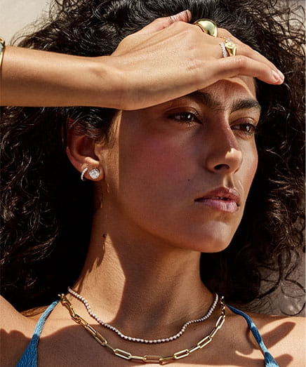 Woman shielding eyes from sunlight wearing earrings and necklaces