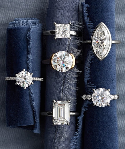 Five diamond rings displayed on blue textured fabric.