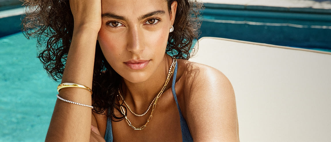 Woman by a pool wearing gold jewelry and a blue swimsuit.
