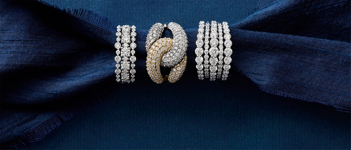 Three diamond-studded rings on dark blue fabric background.