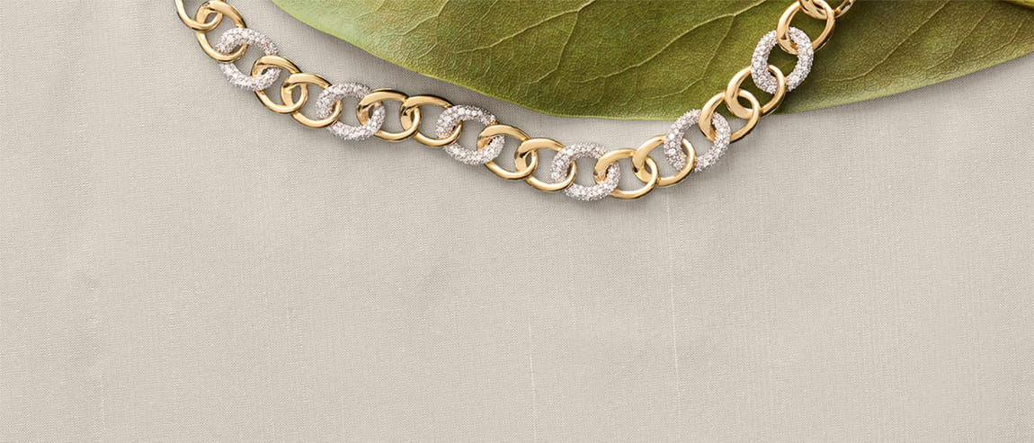 Gold and diamond chain necklace displayed on a green leaf and beige fabric.
