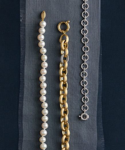 Three bracelets: pearl, gold chain, and silver link, displayed on striped fabric.