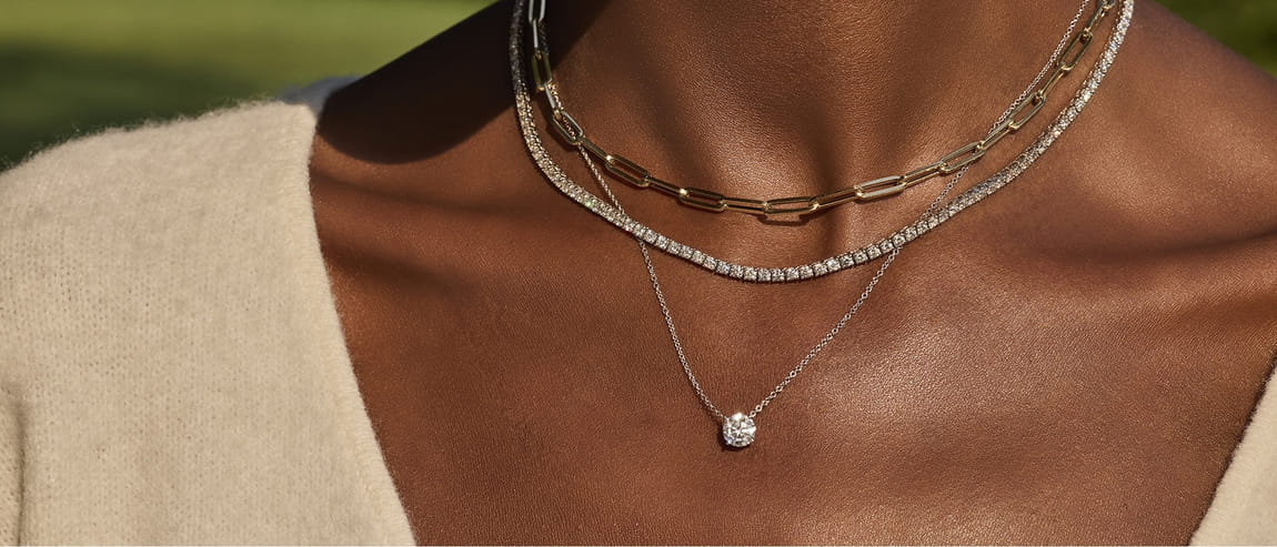 Close-up of a woman's neck with layered gold and diamond necklaces against brown skin.