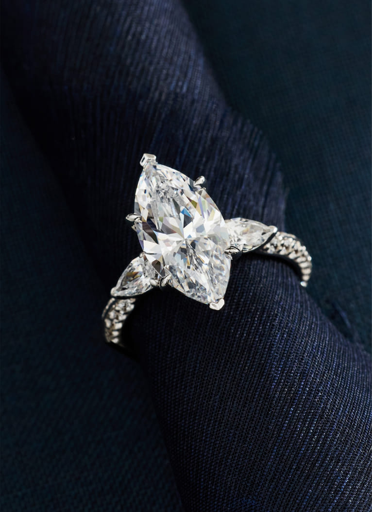 A marquise-cut diamond ring with side stones on a dark fabric background. A marquise-cut diamond ring with side stones on a dark fabric background.