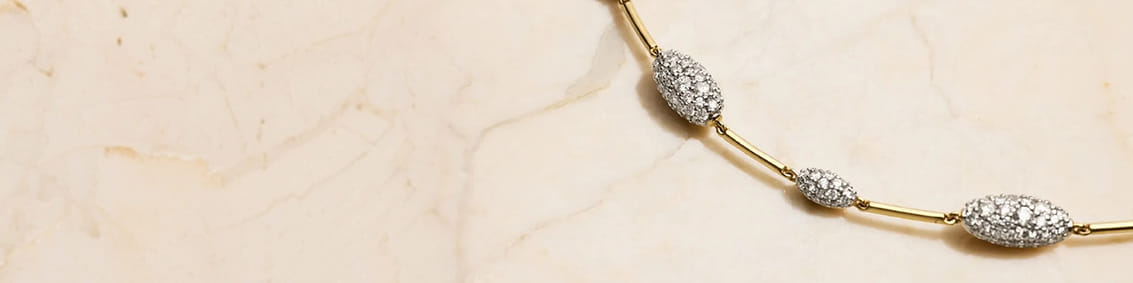 Gold bracelet with diamond-studded beads on a marble background.