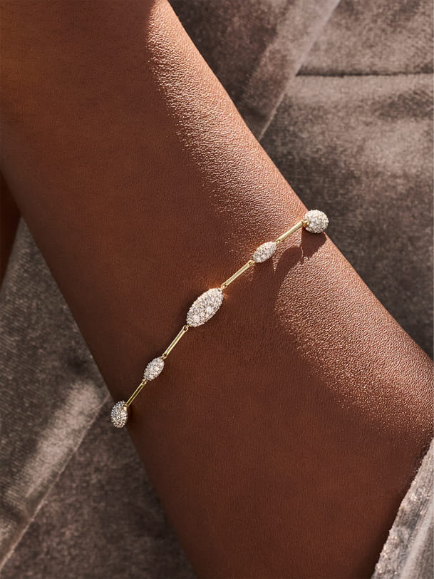 Close-up of a gold bracelet with oval diamond clusters on an arm. Close-up of a gold bracelet with oval diamond clusters on an arm.