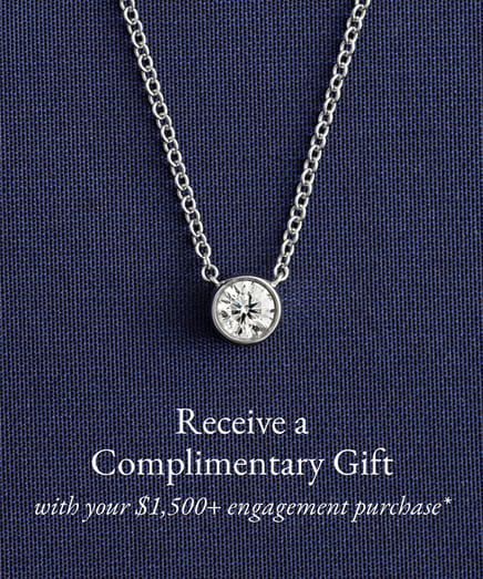 Diamond necklace on blue fabric with offer for complimentary gift with engagement purchase.