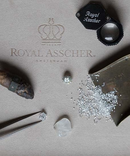Jewelry tools and diamonds displayed on a surface with Royal Asscher branding.