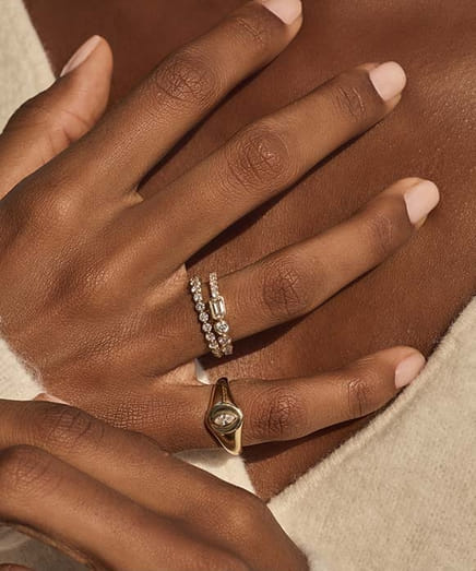 Hand wearing stacked diamond and gold rings on index and pinky fingers.