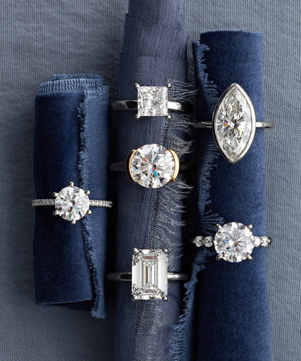 Five diamond rings on blue fabric rolls showcasing various cuts and settings.